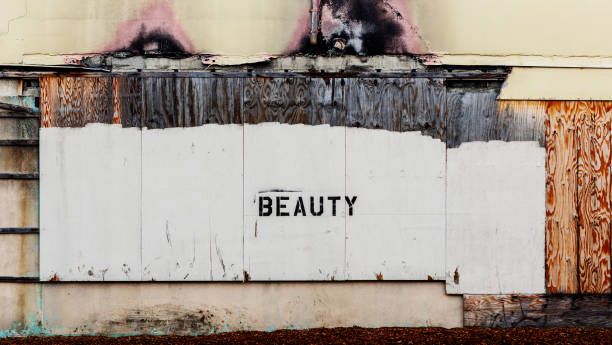 The black letters BEAUTY stenciled on a building wall with wood damaged by fire.