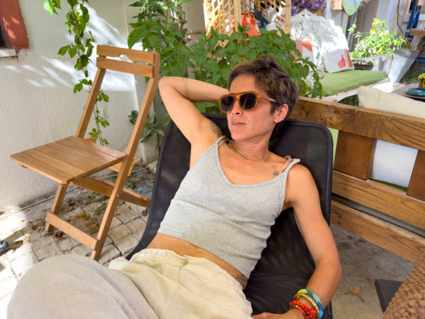 Beautiful adult woman sitting in a cafe. She lives in a cafe in a small town. A comfortable chair. She looks peaceful with her sunglasses. In modern casual clothes. A summer day.