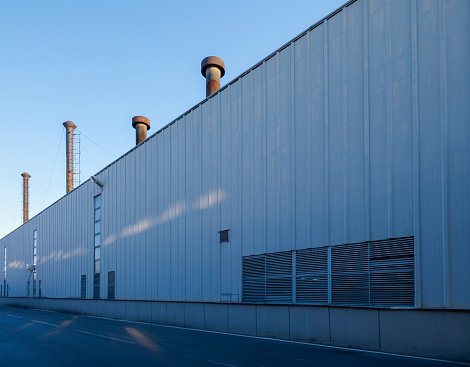 Side view of a modern factory. The exterior of the building is covered with aluminum. A factory producing heavy metal industry. Many chimneys. Ventilation vents. There are no people.