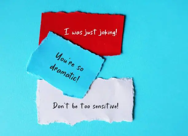 On blue background, torn paper with handwriting I WAS JUST JOKING, YOU'RE SO DRAMATIC and DON'T BE SO SENSITIVE, gaslighting verbal abuse use to manipulate and pin whole blame to victim