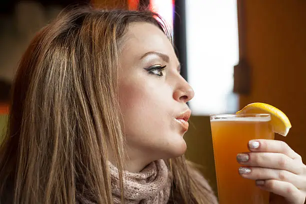 Portrait of a young woman with beautiful blue eyes drinking a pnt of hefeweizen beer.
