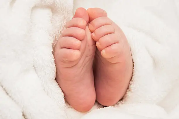 Two babyfeet on white coverlet. Toes. Feet as if in prayer. Horizontal photo. Macro. Close-up.