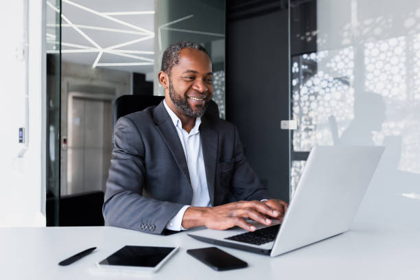 istock Successful african american manager inside office at workplace, man working using laptop smiling and happy with achievement results and financial money, boss in business suit typing on keyboard 1641233747