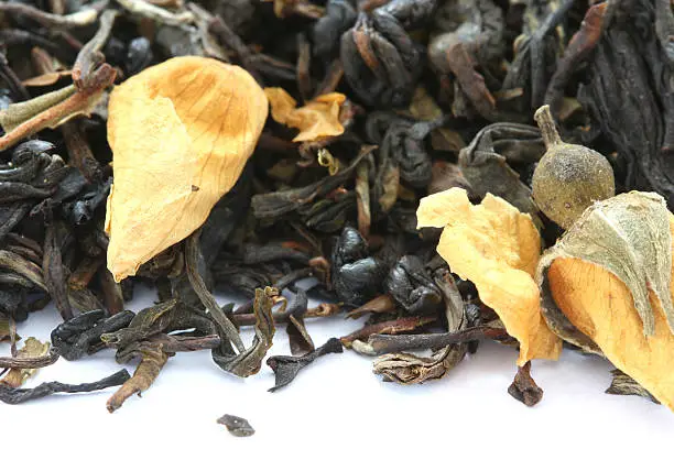 Dry black tea flavored with dry flower buds on white background