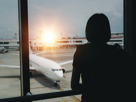 Young woman looking at the plane through the window evening glowing holiday travel