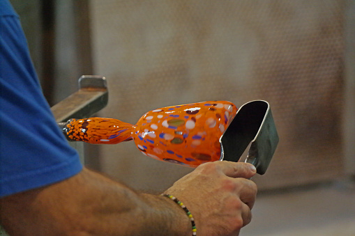 Glass blowing and shaping a wine glass.   Orange glass with colorful spots.