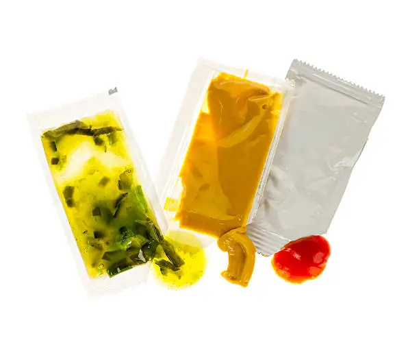 Relish mustard and ketchup condiment packets open on white background