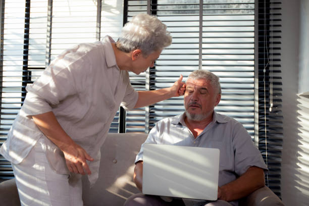 istock Caucasian elderly man working on laptop computer while elderly woman care sitting on sofa while eyestrain for overwork in living room at home, business senior is migraine, business and health concept. 1641452118