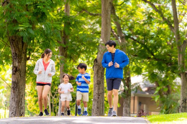 Asian family jogging exercise together at park. Happy Asian parent and little kids enjoy and fun outdoor lifestyle on summer vacation. Father, mother and child jogging workout exercise together at park. Family relationship and health care concept. asian child phycical activity stock pictures, royalty-free photos & images