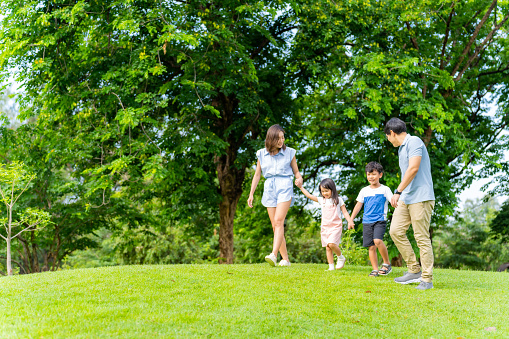 Happy Asian family spending time together on summer holiday vacation. Parents and little child kids enjoy and fun outdoor activity lifestyle walking and playing together at public park in the city.