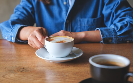 Closeup image of a woman holding and drinking coffee with friend in cafe