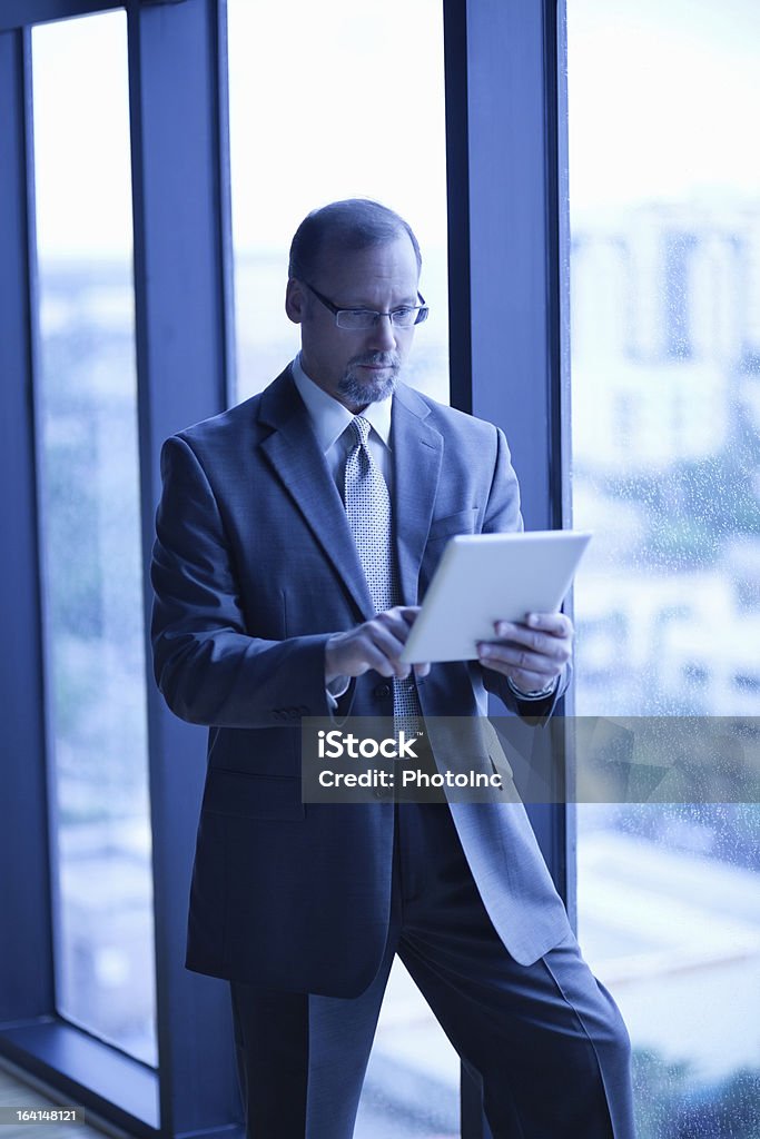 Businessman Using Digital Tablet At Office Mature businessman using digital tablet by glass window at office 50-54 Years Stock Photo