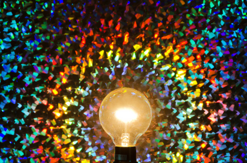 A colorful multicolored abstract background and a clear yellow light bulb. Rainbow colors.
