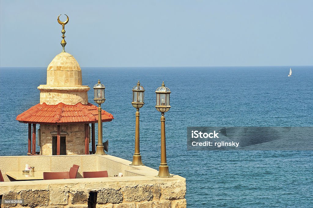 Old mosque. Yafo, Israel. Small restaurant's stone balcony with lanterns and minaret of old mosque against background of Mediterranean sea in Yafo, Israel. Street Light Stock Photo