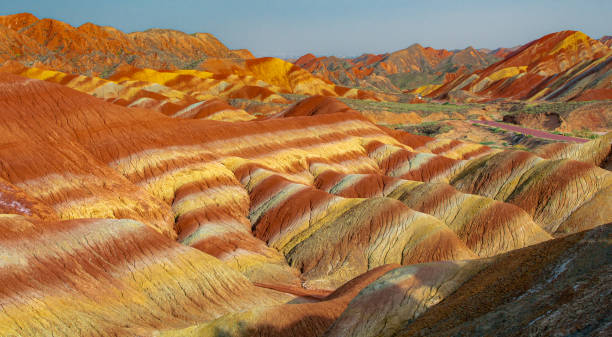 The road through the typical Danxia land form in Zhangye Danxia Park, China The road through the typical Danxia land form in Zhangye Danxia Geological Park, Zhangye, Gansu, China. Blue sky with copy space for text, colorful, panorama danxia landform stock pictures, royalty-free photos & images