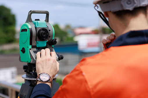 close up and sport focus at equipment theodolite, Surveyor engineer wearing safety uniform and helmet with equipment theodolite to measurement positioning on the construction site of the new road,