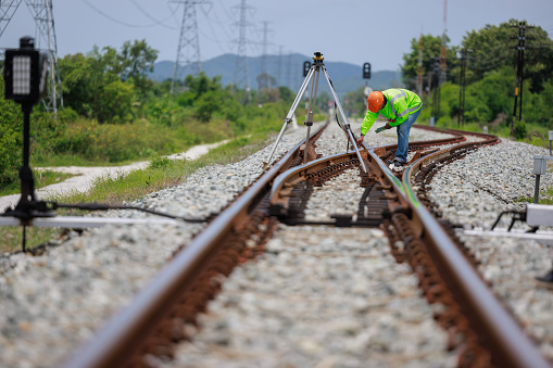 Engineer wearing hard hats and uniforms use theodolite equipment surveying construction worker on Railway site.