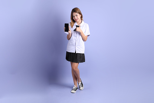 The Asian girl in Thai student uniform standing on the purple background.