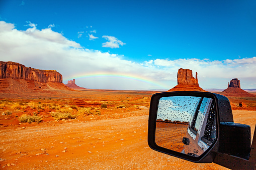 The car mirror reflects the scenic landscape. The famous rock Mitten and the bright rainbow. USA. Navajo Indian Reservations. Monument Valley