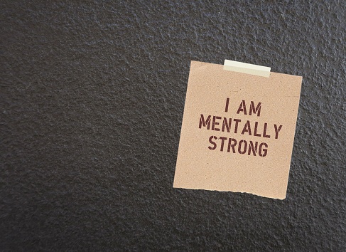 Note stick on dark wall with text I AM MENTALLY STRONG, to remind self to have positive self-esteem to gain ability to take risks, try new things, and cope with life difficult situations