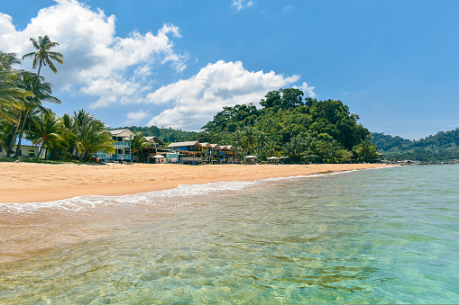 View of the tropical beach of tioman island. Crystal clear sea, beautiful golden sand beach with traditional houses and green palm trees. An ideal photo for the promotional purposes of a travel agency.