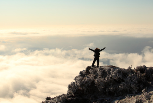 Woman standing on top of the mountain with his hands raised