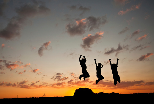 A silhouette of three young boys jumping. Horizontal colour image.