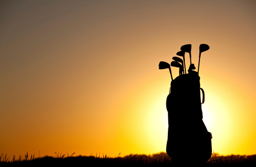 A golf bag silhouette. Horizontal colour image. Copyspace. Sunset. Golf equipment with sun behind. Equipment includes drivers, irons, putters, wedges, and golf cart bag. Course is a beautiful links golf course in Scotland. Nobody is in the image, shot with Canon 5D Mark II.