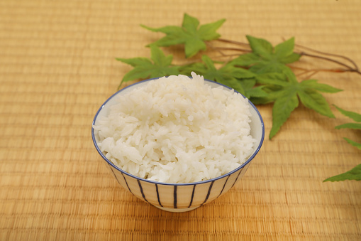 Japanese rice in a bowl on a brown wooden background with green leaf