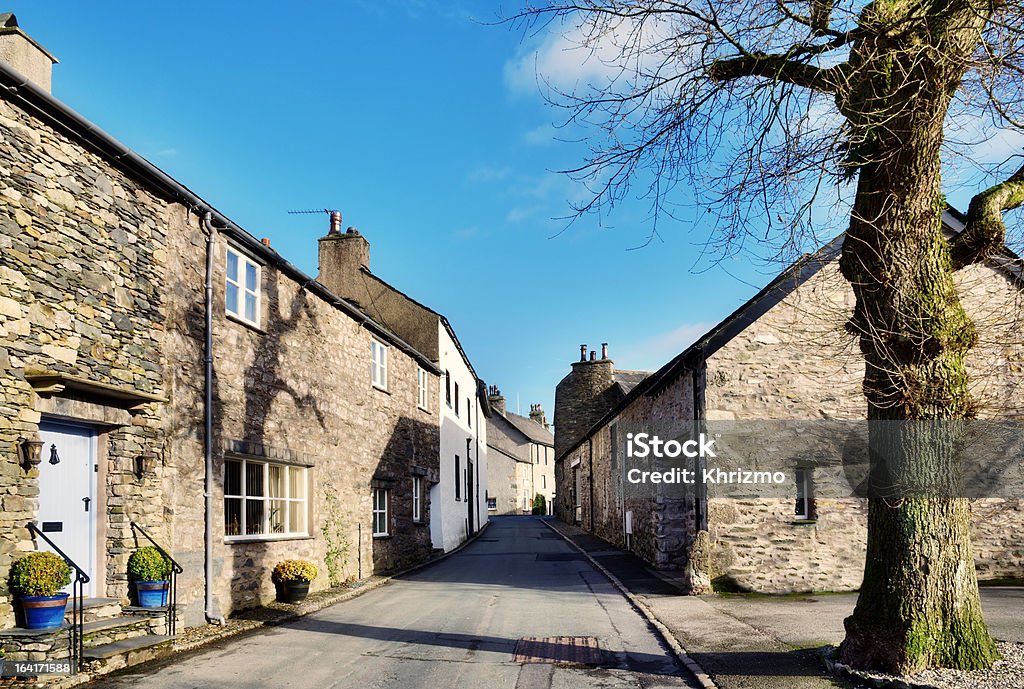 View of a street in Cartmel, Cumbria with tree View of a picturesque street with cottages, and a tree set against a blue sky, in the village of Cartmel, Cumbria, England, on a sunny winter afternoon. Cartmel Stock Photo