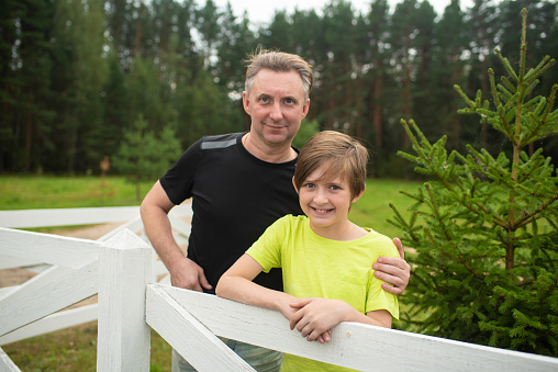 portrait of a father with a 10 year old son near a white fence in summer