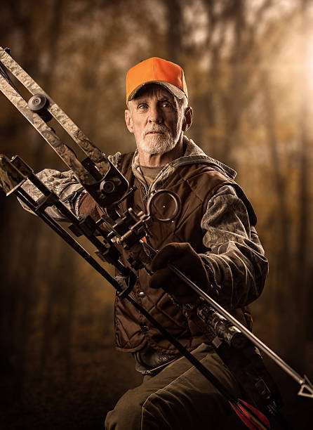 Bearded older male hunter with a crossbow Hunter in the woods with bow and arrow ready to take aim at his prey. archery bow stock pictures, royalty-free photos & images