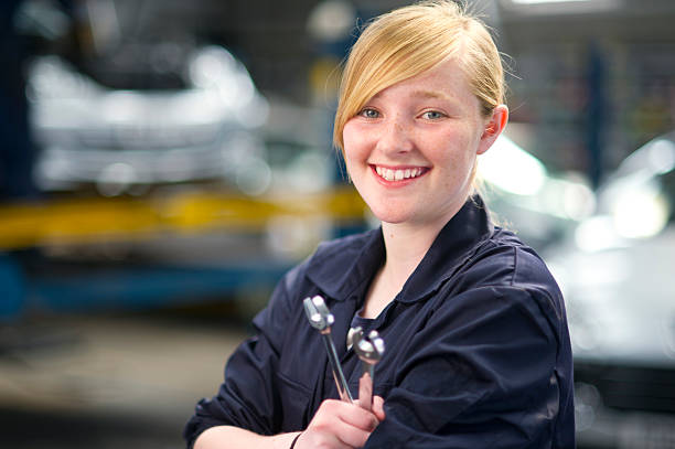 Female mechanic working at the auto repair shop, she is checking a car engine and smiling at camera