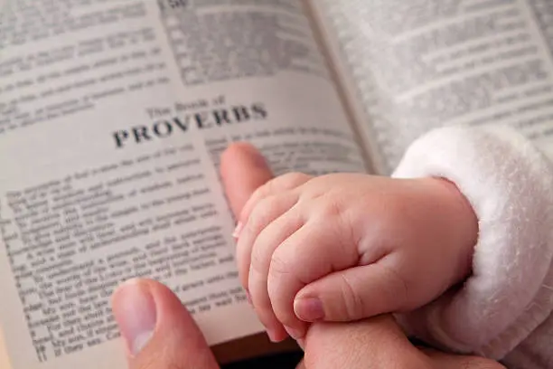 Baby holding father's finger as he points to Proverbs verse