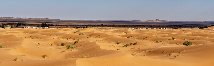 Sand dunes landscape in the Moroccan desert Erg Chebbi with tent camps in the background.