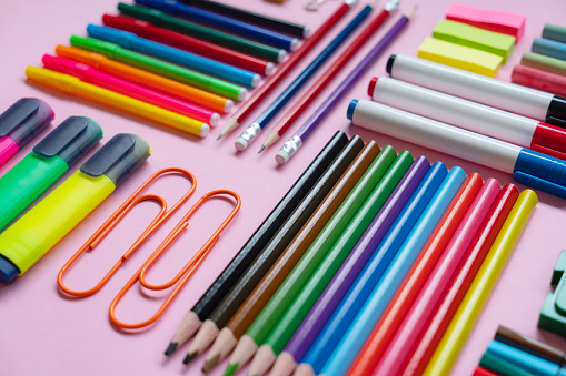 Office and school supplies arranged on pink background