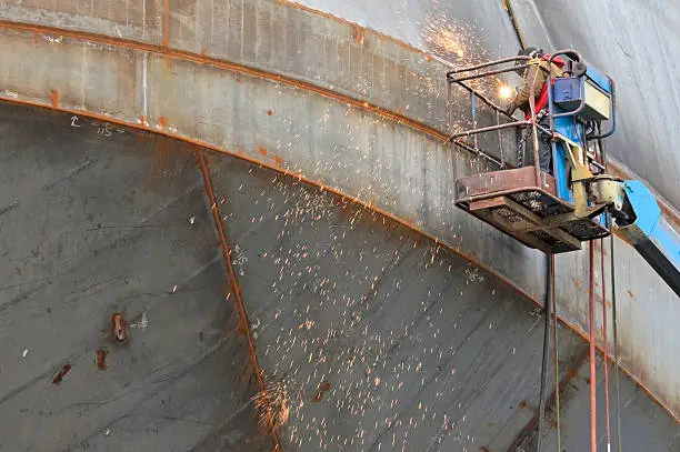 Man welding seams on hull of ship under construction in drydock