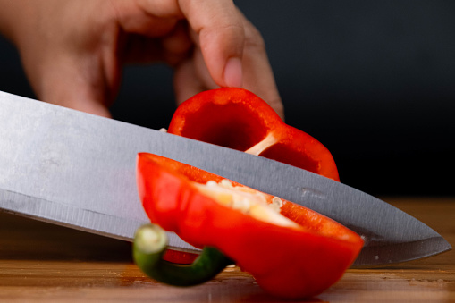Hands cutting red bell peppers on a wooden chopping board. Woman chopping bell peppers in kitchen close up.
