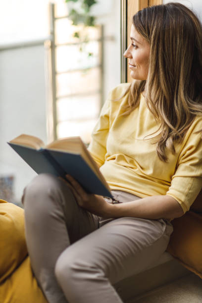 istock Woman relaxing on the window sill and reading a book 1641956845