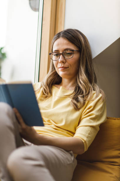 istock Woman relaxing on the window sill and reading a book 1641956853