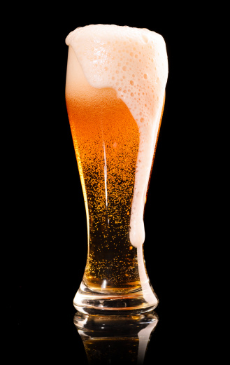 overflowed glass of fresh lager beer on black with reflection