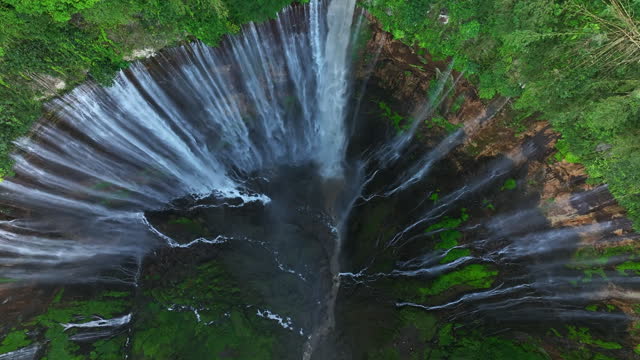 Aerial view descending and tilting up to reveal Tumpak Sewu waterfall, Indonesia