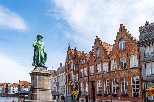 Jan Van Eyck Square and Monument in Bruges. Canal Spiegelrei and Flemish buildings in the background in summer.