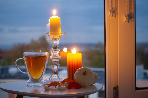 glass cup with tea and burning candles on background window with autumnal landscape