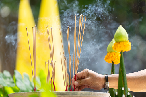 Man's hand inserting prayer incense into a cauldron many incense sticks smoke