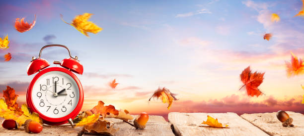 Fall Back Time - Daylight Savings End - Clock Alarm At Sunrise With Leaves - Return To Winter Time stock photo