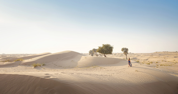 Desert adventure. Young arabian Woman in sexy boho blue makrame dress in sands dunes of UAE desert at sunset. The Dubai Desert Conservation Reserve, United Arab Emirates.