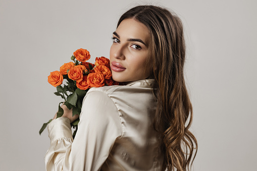 Portrait of a beautiful young woman holding a bouquet of orange color roses, studio shot in front of a white background