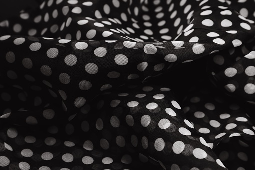 A close-up of black fabric with a white polka dot pattern visible on its surface