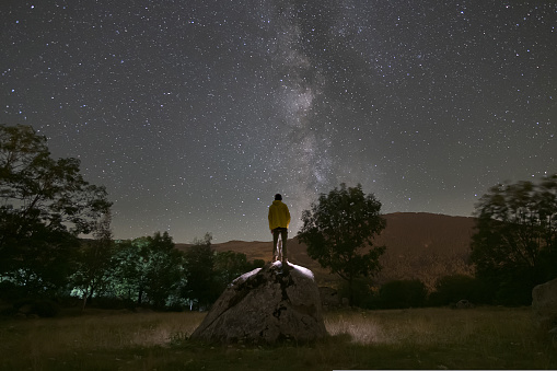 rear view of man climbed on a rock looking at the milky way at night. High quality photo